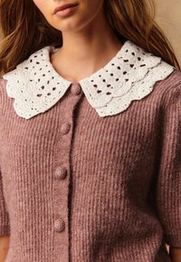 Gebreide cardigan van zachtroze wol met een geribbelde textuur, voorzien van een grote witte kanten kraag en ronde knopen aan de voorkant.