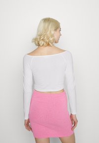 Top crop branco de mangas compridas com decote off-the-shoulder, combinado com uma saia mini pink ajustada e texturizada.