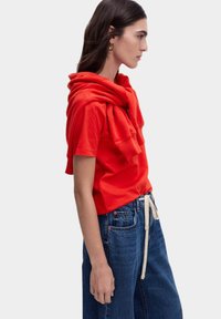 Rode T-shirt met korte mouwen en een capuchon die over de schouders hangt, gecombineerd met wijde blauwe denim jeans. Soepele stof, casual pasvorm.