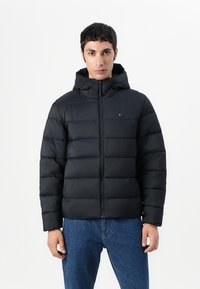 Black puffer jacket with a hood, featuring quilted sections, zip closure, and a small logo accent. The fabric has a smooth, shiny texture.