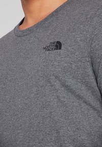 Camiseta gris de manga corta hecha de mezcla de algodón, con escote redondo y logo negro en el pecho izquierdo. Textura suave con un ajuste casual.