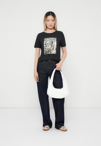 Zwarte t-shirt met een glanzend zilveren pailletten vierkant ontwerp, gecombineerd met donkerblauwe wijde jeans en een witte schoudertas met studs.