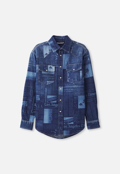 Camisa de ganga em várias tonalidades de azul, apresentando padrões de impressão de jornal, dois bolsos no peito e fechos de botão de pressão. Design clássico de colarinho.