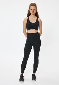 Sort sports-bh og højtaljede leggings i et glat, strækbart stof; leggings har et subtilt stjernemønster nær anklen.