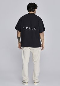 Melnas pārmērīgas T-krekls ar baltiem "SIKSILK" uzrakstiem, kombinēts ar krējuma krāsas biksēm. Iekļaujapaļa kakla izgriezumu un īsās piedurknes.