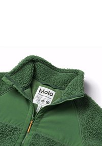 Giacca in pile verde con colletto alto, chiusura con zip e pannelli testurizzati a contrasto. Presenta un'etichetta con messaggi eco-sostenibili.