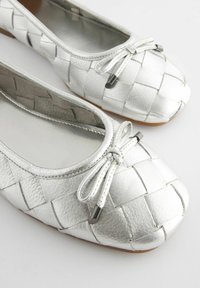 Hopeakattoiset nahka-ballet-shoet, joissa on kudottu muotoilu, nauhaakcentti varvassa, litteät pohjat ja sileä sisävuori.