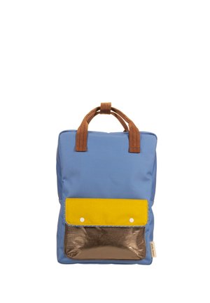 Sac à dos bleu avec des poignées marron, une poche avant avec une base métallique marron et un rabat jaune maintenu par deux boutons blancs.