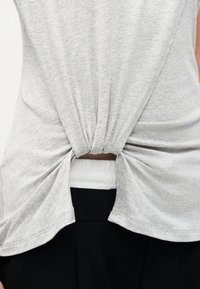 Γκρι τοπ, μαζεμένο και στριφογυριστό στο πίσω μέρος της μέσης, αποκαλύπτοντας ένα μικρό τμήμα λευκού υφάσματος πάνω από μαύρο κάτω μέρος.