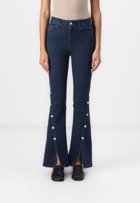 Jeans de campana de color azul oscuro con cintura alta, bolsillos delanteros, detalles de botones a lo largo de las costuras laterales y dobladillos divididos en los tobillos.