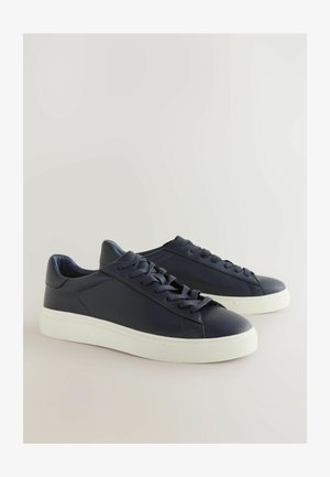 Sötétkék bőrsneaker, textúrázott felülettel, fehér gumitalppal és lapos fűzőkkel. Egyszerű dizájnnal rendelkezik, minimális varrási díszítésekkel.