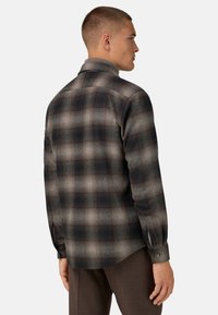 Camisa de franela con un patrón de cuadros en gris oscuro y negro, mangas largas, puños abotonados y cuello extendido. Textura suave y ajuste flexible.
