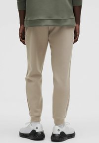 Beige sweatpants med en afslappet pasform, der har elastiske manchetter. Kombineret med hvide træningssko med sorte sprøjtede såler og logo detaljer.