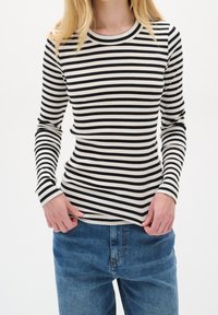 Maglia a righe bianche e nere a maniche lunghe con scollo tondo, abbinata a jeans di denim blu. Vista ravvicinata del torso.