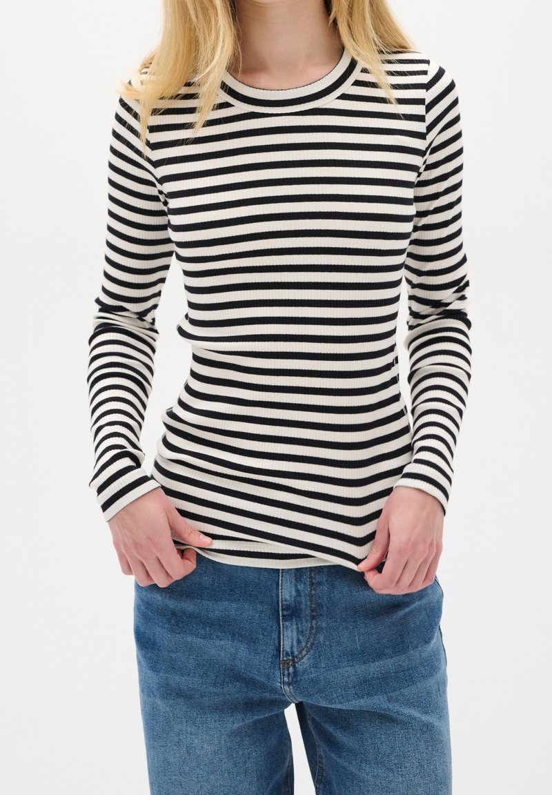 Maglia a righe bianche e nere a maniche lunghe con scollo tondo, abbinata a jeans di denim blu. Vista ravvicinata del torso.