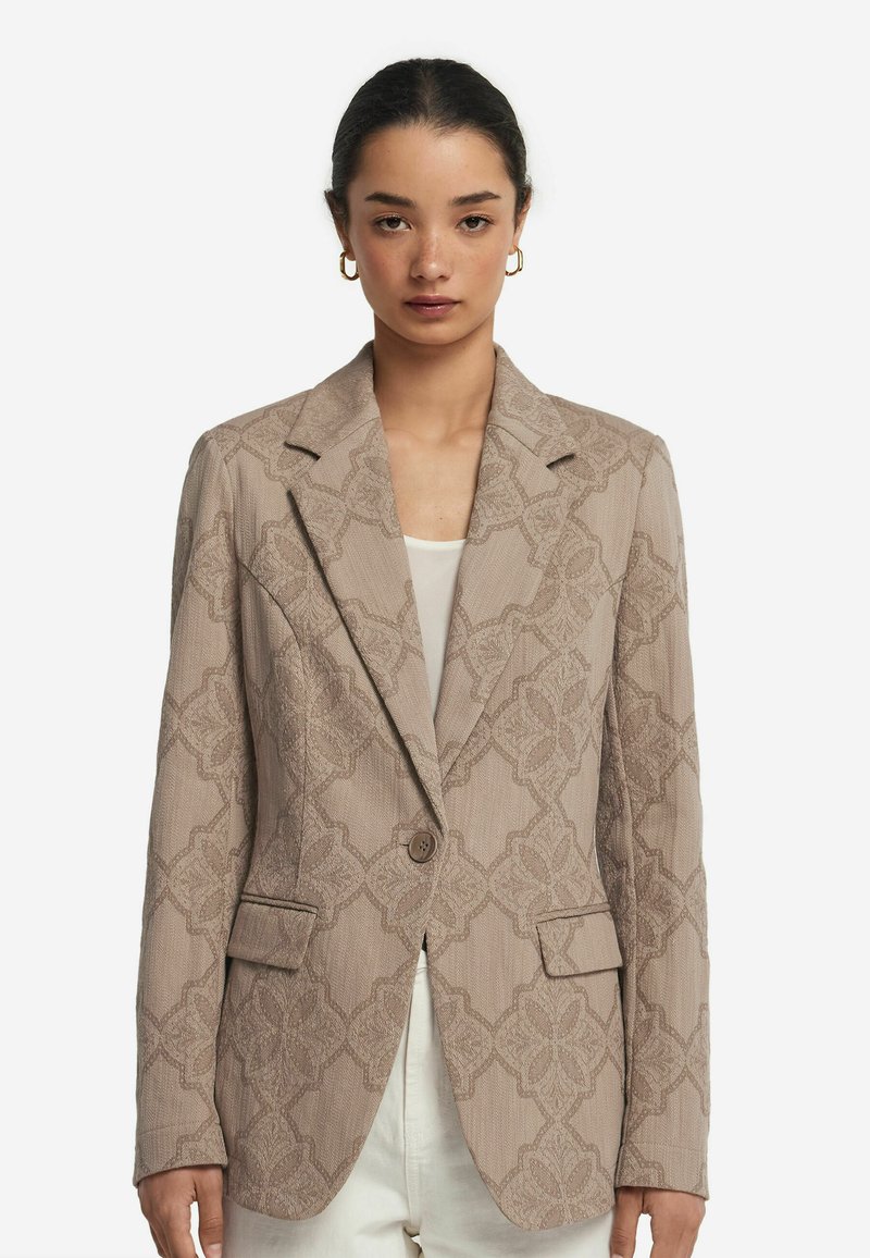 Blazer beige texturé avec un léger motif floral, fermeture à un bouton, revers crantés et deux poches avant.