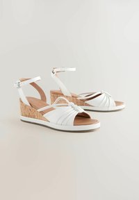Sandales compensées blanches avec un design noué, talon en liège et bride de cheville réglable. Matériau lisse ressemblant à du cuir avec une couleur unie.