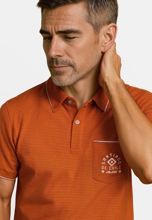 Polo shirt orange à rayures avec col boutonné, manches courtes et une poche sur la poitrine gauche arborant un texte et des détails de design blancs.