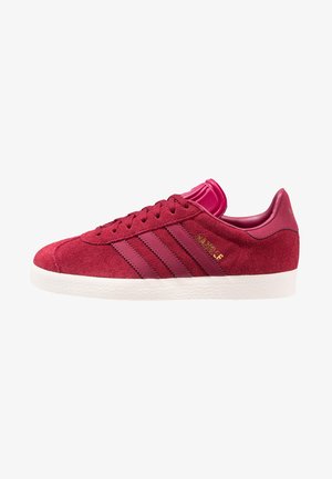Basket Adidas Gazelle en daim rouge avec des bandes rouge foncé, une semelle blanche et un texte doré "Gazelle" sur le côté, vue de profil extérieur.