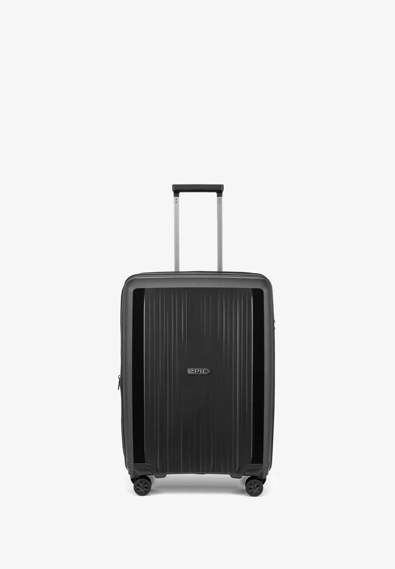 Harde koffer met een geribbelde zwarte buitenkant, zilveren telescopische handgreep en vier zwarte wieltjes. De voorkant heeft een logo.