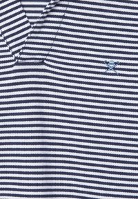 Polo rayé bleu marine et blanc avec un col en V. Présente un petit accent brodé, une texture douce et un design décontracté.