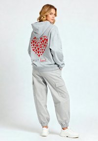 Felpa grigia con stampa a cuore rosso e testo "SWEET heart" sul retro. Abbinata a pantaloni cargo grigi chiari e sneakers bianche.