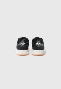 Black sneakers with a round toe, fabric upper, white midsole, and rubber outsole. Features a small logo on the back and textured accents.