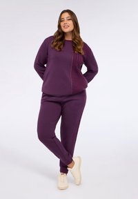 Felpa viola con motivo testurizzato su un lato e pantaloni della tuta viola coordinati. Il tessuto sembra morbido e confortevole, con dettagli a coste.