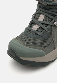 Grüner Wanderschuh aus strukturiertem Mesh und Wildleder, mit Gummizehenkappe und grauen Akzenten. Verfügt über eine Schnürschlusstechnik und eine langlebige Sohle.