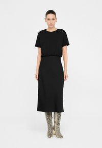 Rochie midi neagră cu mâneci scurte și talie elastică. Modelul poartă cizme până la genunchi cu imprimeu de șarpe metalic. Design simplu și minimalist.
