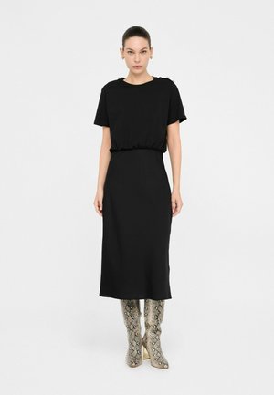 Abito nero midi con maniche corte e vita elastica. Il modello indossa stivali alti fino al ginocchio con stampa serpente metallica. Design semplice e minimalista.