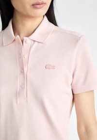 Rosa polo t-shirt med en texturerad tyg, treknaps knäppning och en broderad logotyp på vänster bröst. Korta ärmar och slim fit-design.