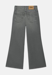 Šedé kalhoty s širokým nohavicemi a texturovaným povrchem, s hnědou koženou etiketou s nápisem "TOMMY HILFIGER" a dvěma zadními kapsami.