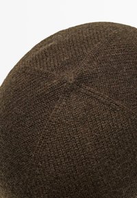 Cappello lavorato a maglia marrone con una texture liscia. La corona arrotondata presenta un motivo esagonale cucito, che mette in mostra un design a tinta unita.
