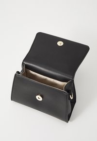 Sac à main en cuir noir avec un fermoir à pression doré, un intérieur spacieux et une doublure beige douce. Présente un design structuré et un matériel minimaliste.