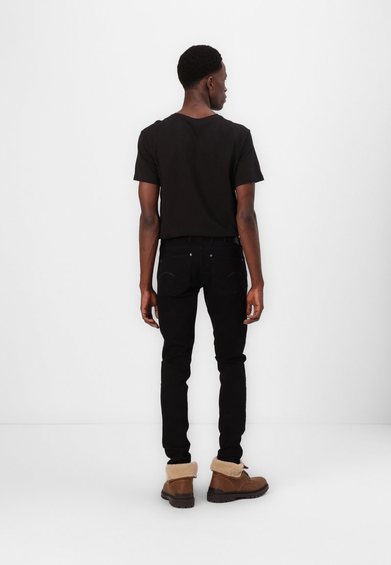 T-shirt noir à col rond, jeans noirs ajustés et bottes marron avec un revers en fourrure beige. Design minimaliste sans logos visibles.