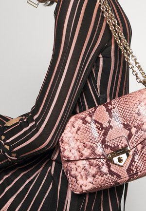 Person iført en sort og pink stribet dragt, der holder en pink håndtaske med slangeskindsmønster og guldkæde som rem.