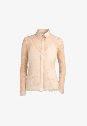 Blouse beige à manches longues en dentelle florale avec col uni, patte de boutonnage et doublure intérieure de type combinaison sur le haut de la poitrine.