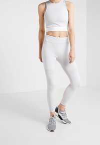 Top corto deportivo blanco y leggings con inserciones de malla, fabricados con un material elástico. Combinados con zapatillas de correr grises para un aspecto deportivo.