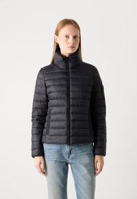 Doudoune noire avec un col haut, design matelassé horizontal et fermeture éclair. Comprend des poches latérales et une texture lisse et brillante.