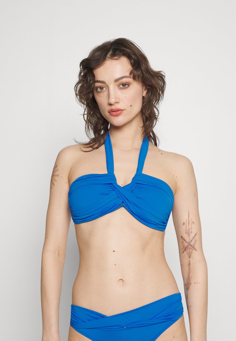Bikini blu con bandeau e collo alla halter, caratterizzato da dettagli di tessuto arricciato al centro. Texture liscia, set a due pezzi con slip coordinato.