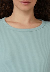 Mintgrünes, geripptes Oberteil mit rundem Ausschnitt. Der Stoff wirkt weich mit feinen vertikalen Texturen. Einfaches Design ohne zusätzliche Verzierungen.