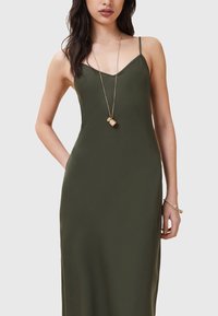 Vestido maxi sin mangas en verde oliva con escote en V, confeccionado con una tela suave. Presenta un ajuste ceñido y bolsillos laterales, complementado con un collar dorado.