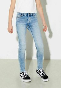 Ljusblå skinny jeans i denimtyg, med fem fickor, blekta områden och medelhög midja, tillsammans med svart och vit sneakers.
