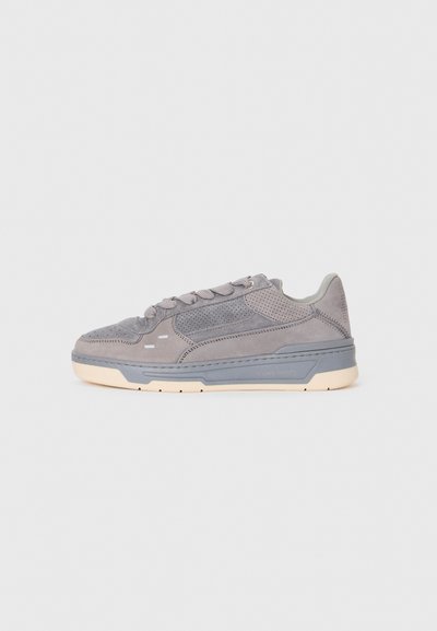 Szare zamszowe sneakersy z perforowanymi detalami, gruba szara podeszwa środkowa, kremowa podeszwa zewnętrzna oraz zapięcie na sznurówki, pokazane w profilu bocznym na białym tle.