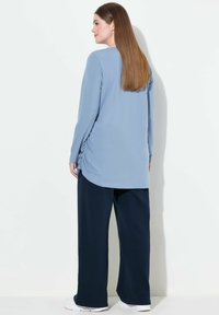 Top azzurro chiaro a maniche lunghe con scollo rotondo e arricciature laterali, abbinato a pantaloni larghi blu navy. Tessuto morbido, vestibilità casual.