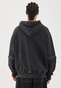 Overdimensjonert svart hettegenser med snorhette, ribbestrikkede mansjetter og liv; laget av myk, teksturert stoff med en slitt finish.