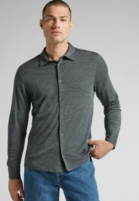 Langarmige blouse in donkergrijze gestructureerde stof. Heeft een kraag, knopen aan de voorkant en een relaxed fit, gecombineerd met blauwe jeans.