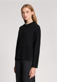 Czarny sweter z miękkiego materiału dzianinowego, z ribbowanym dołem, okrągłym dekoltem i długimi rękawami. Model jest luźny, z teksturowanym wykończeniem.