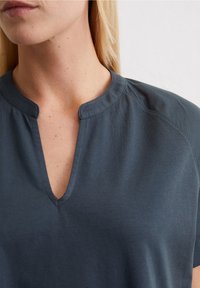 Mörkblå T-shirt med V-ringning och korta ärmar, tillverkad av mjukt tyg; har en avslappnad passform och subtila sömnadsdetaljer nära halsringningen.